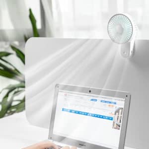 A portable USB desk fan with a magnetic clip, featuring a white design and a round grille, positioned near a laptop.