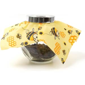 A beeswax wrap in yellow with a bee and honeycomb design covering a glass jar filled with dark contents.