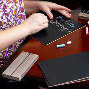 A set of tabletop chalkboard signs with a wooden base, accompanied by colourful chalk pieces, on a wooden table.