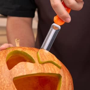 A pumpkin carving kit featuring a silver carving tool with an orange handle, used to shape a Halloween pumpkin.