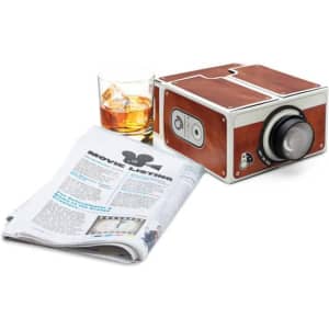 A cardboard smartphone projector in brown and silver, next to a glass of whiskey and a newspaper.