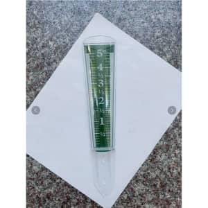 A clear, plastic magnifying rain gauge in green, displaying measurements from 0 to 5 inches on a flat surface.