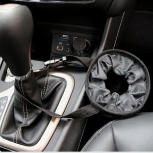 A black car seat back garbage bag with a strap, positioned beside a gear shift in a vehicle interior.