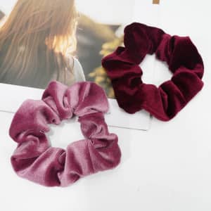 A pair of soft velvet scrunchies in pink and burgundy, placed on a magazine with a blurred background.