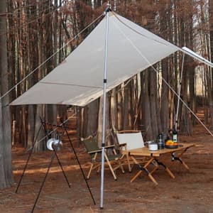 An adjustable camping tarp set up with a white tarp, silver poles, and outdoor furniture in a forest setting.
