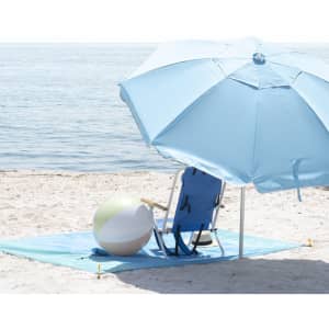 A blue beach umbrella stands beside a beach chair and a brightly coloured beach ball on sand near the water.