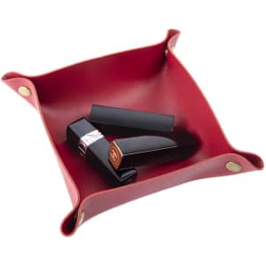 A red foldable leather storage tray with black lipstick tubes inside. The tray features metal corners and branding.