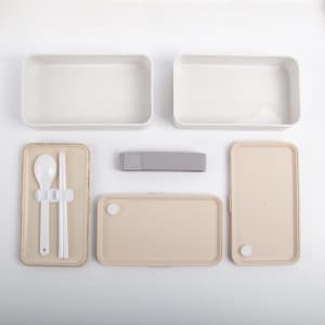 A double-layer lunch box in beige and cream, including utensils, a strap, and two separate containers.