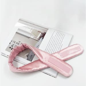 A pink silk headband with a smooth texture, displayed beside a magazine on a white surface.