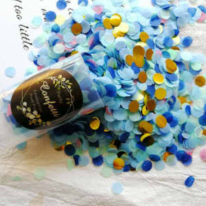 A clear tube filled with blue and gold confetti, surrounded by scattered pieces of the same confetti on a white background.
