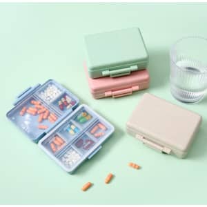 A set of custom wheat straw pill cases in green, pink, and beige, with a glass of water beside them.