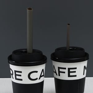 Two biodegradable disposable drinking straws in brown, placed in black cups with white text.