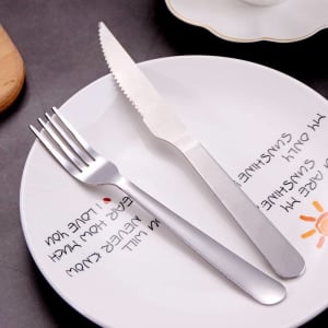 A stainless steel cutlery set featuring a fork and knife on a decorative plate. The cutlery has a polished finish.