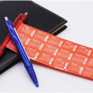 A blue retractable advertising banner pen alongside a red pen, placed on a black notebook with a calendar strip.