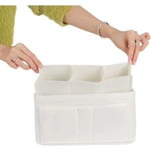 A felt purse organiser in cream with multiple compartments, held by a hand. It has a simple design and a logo.