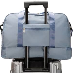 A large capacity travel duffel bag in blue, featuring a front pocket and placed on a wheeled suitcase.