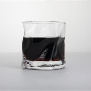 A clear, irregular whiskey glass filled with dark liquid, featuring a sleek, wavy design.