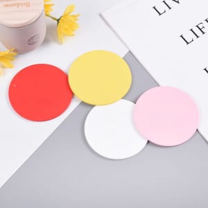 A set of four round coasters in red, yellow, pink, and white, featuring a smooth surface and a branding logo.
