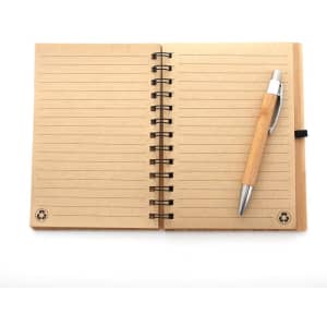 A bamboo spiral notebook with lined pages and a silver ballpoint pen resting on top. The notebook features a logo.