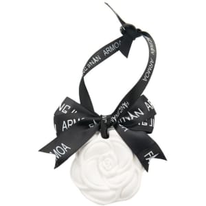 A white hanging aromatherapy tablet in the shape of a flower, tied with a black ribbon. Features a logo on the ribbon.