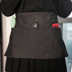 A grey custom half apron with pockets, displaying kitchen utensils like a spatula, fork, and spoon.