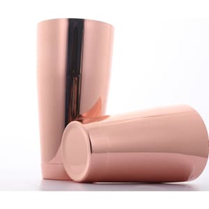 A cocktail shaker set in rose gold finish, featuring two sleek and shiny metallic pieces with a branding logo.