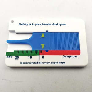 A white keychain tyre depth measuring ruler with a blue measuring slider, featuring safety indicators and a logo.
