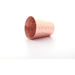 A hammered copper shot glass with a shiny finish, featuring a textured surface and a rounded shape.