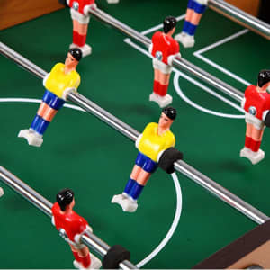 A tabletop football game featuring red and yellow player figures on a green pitch with silver rods.