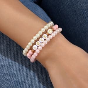 A set of three stretch plastic bracelets featuring pink and white beads, with one bracelet displaying the word "LOVE."