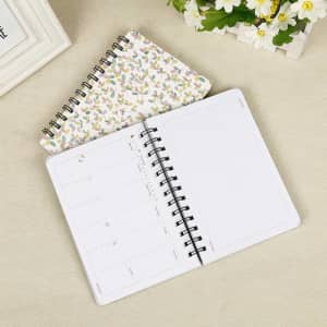 A B6 hardcover planner spiral journal with a floral cover. It features blank and laid-out pages inside.