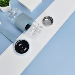 A drink bottle made of clear borosilicate glass, featuring a light blue silicone sleeve and a matching lid.