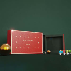 A red custom gift box with a greeting card set, featuring gold detailing and decorative mini toys on a green background.