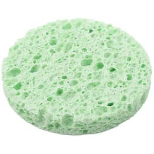 A round facial sponge in a light green colour, featuring a porous texture. The image has a branding logo.