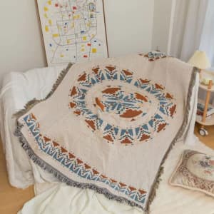 A knitted throw blanket with tassels in beige, blue, and rust colours, featuring a circular pattern.