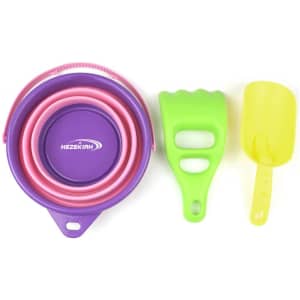 A foldable sand bucket set in purple, pink, and green, featuring a bucket, a shovel, and a rake. Includes a logo.