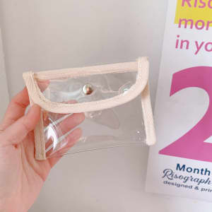 A clear coin purse with a cream-coloured trim and a snap closure, held against a plain background.
