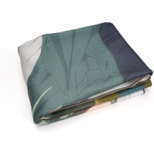 A folded coral fleece throw blanket featuring a printed design in green and other soft colours. It includes a logo.