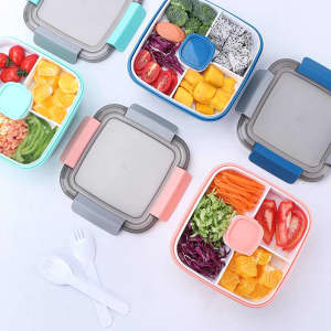 Four colourful lunch containers are arranged, featuring compartments with fresh vegetables, fruits, and a bowl for salad.