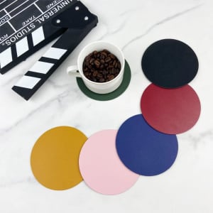 A drink bottle rests on a green PU leather non-slip coaster, surrounded by coasters in black, red, blue, pink, and yellow.