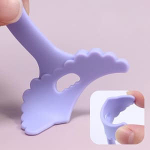 A lavender silicone tool with a scalloped edge, designed for makeup application, featuring a handle and a small cut-out.