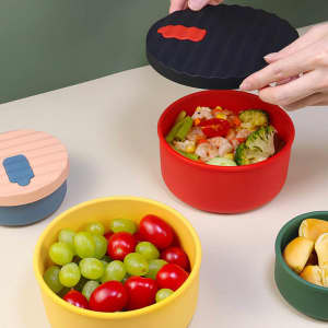 A collection of food grade round silicone lunch boxes in red, yellow, and green, featuring matching lids and fresh ingredients.