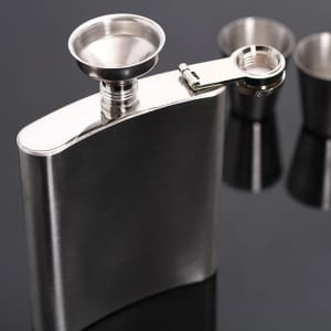 A stainless steel hip flask with a funnel and two shot glasses, set against a dark background.