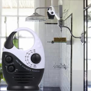 A black and white mini waterproof shower radio with knobs, placed near a showerhead in a bathroom setting.