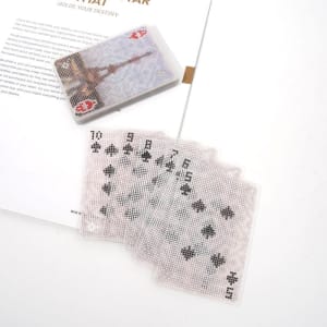 A set of clear PVC playing cards displayed beside the cardbox, featuring a design on the backing and various card faces.