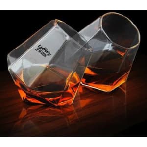 A pair of diamond-shaped, stemless wine glasses with a transparent design and an amber liquid inside.