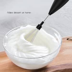 A stainless steel electric egg whisk with a black handle, whisking cream in a glass bowl.