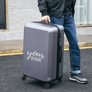 A grey 20-inch carry-on luggage with a simple design is being held by a person on a street.