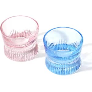 Two crystal whiskey corset glasses, one in pink and one in blue, featuring ribbed designs. Both have a logo.