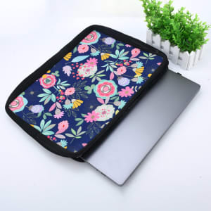 A navy zippered neoprene laptop sleeve features a floral design, with a laptop partially inside and a small plant in the background.